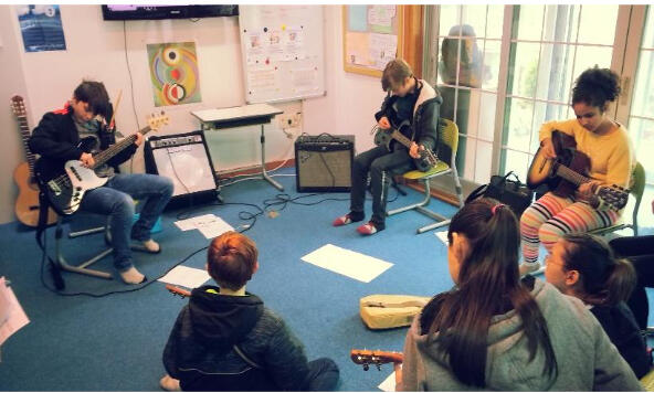 A group of students at British International Academy in Geoje playing guitar together in a music classroom during arts education.